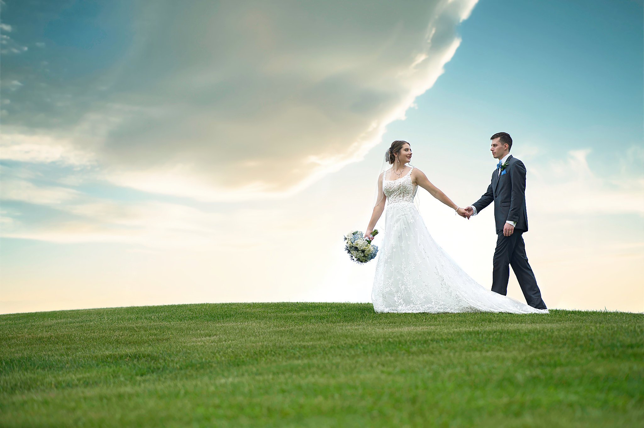 Bride and groom on green hillside under dramatic sky